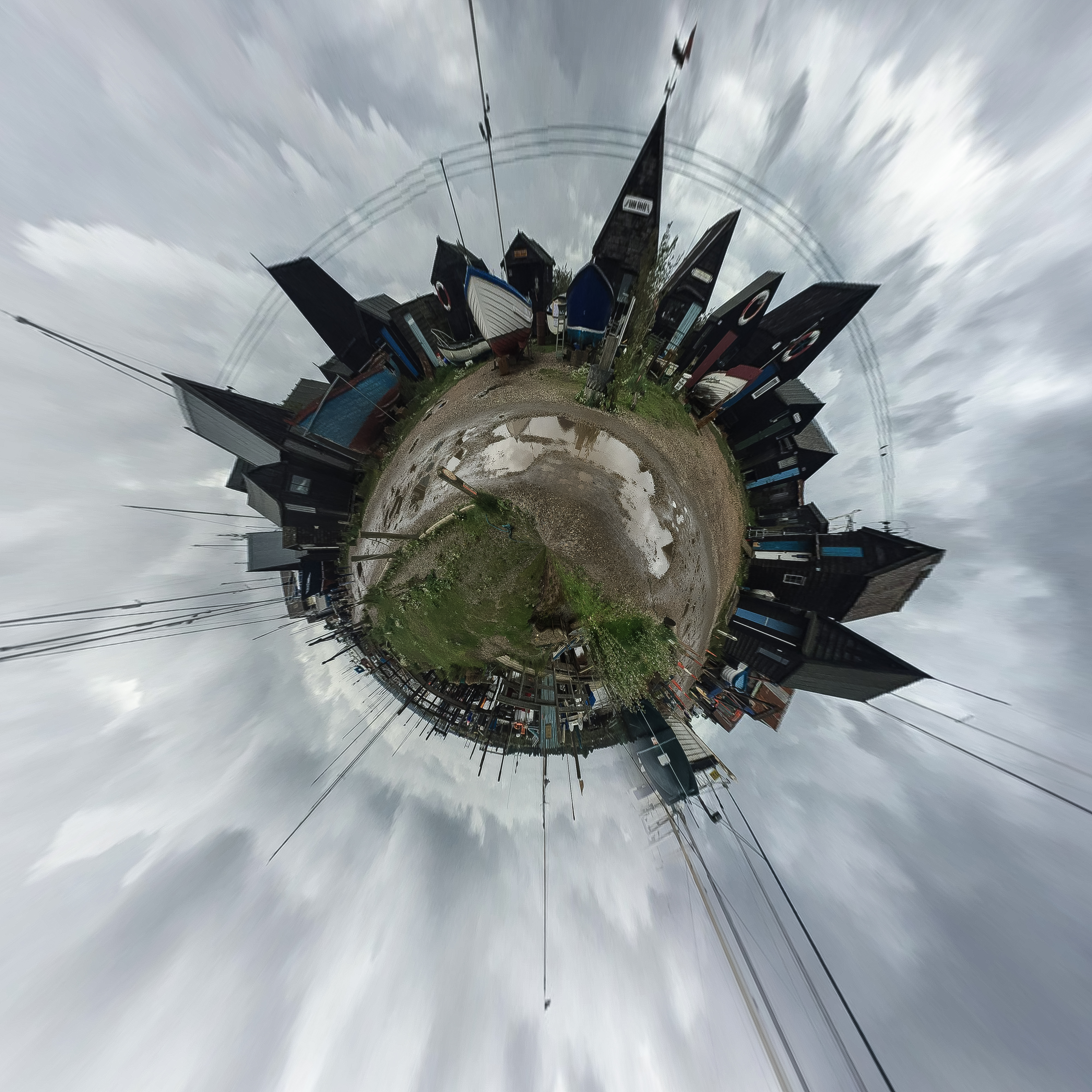 A circle of pointed sheds and thin masts of fishing boats surrounded by a washed out grey sky.