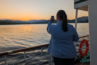 A passenger standing on deck taking a photograph of a sunset from the outer decks off a steamer