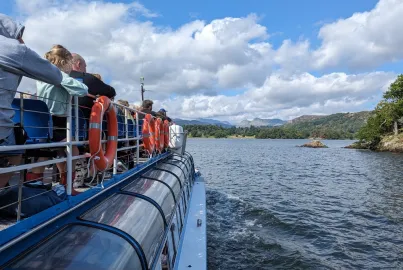 A crowd of people seated on a modern launch upper deck, looking at views across Windermere.