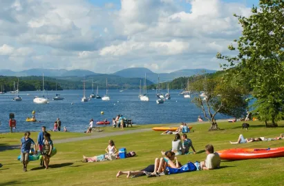 A selection of people relax on the lawns sloping down to the lakeshore