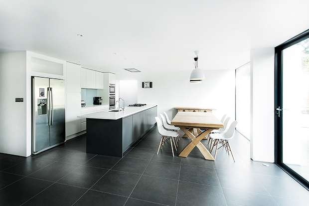 a matte white kitchen with large format grey floor tiles in an extension to a family home