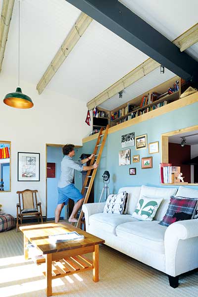 man reaching to mezzanine level with bookcases in converted youth club home