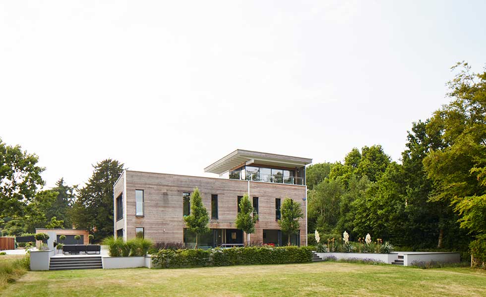 wooden panelled square shaped contemporary home in large green open space