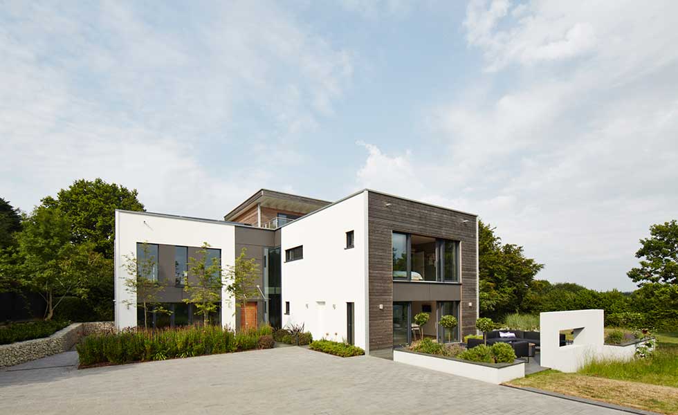 square shaped modern home with white walls and wooden panels and long driveway