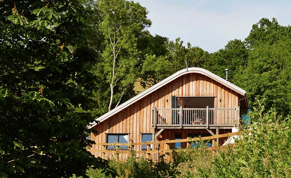 curved roof wooden panelled home with balcony and surrounded by green space
