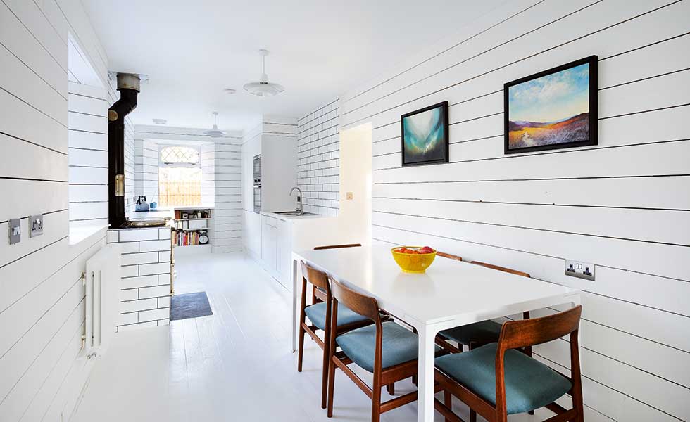 scandi style open plan room with white panelled walls, dining table and wooden chairs