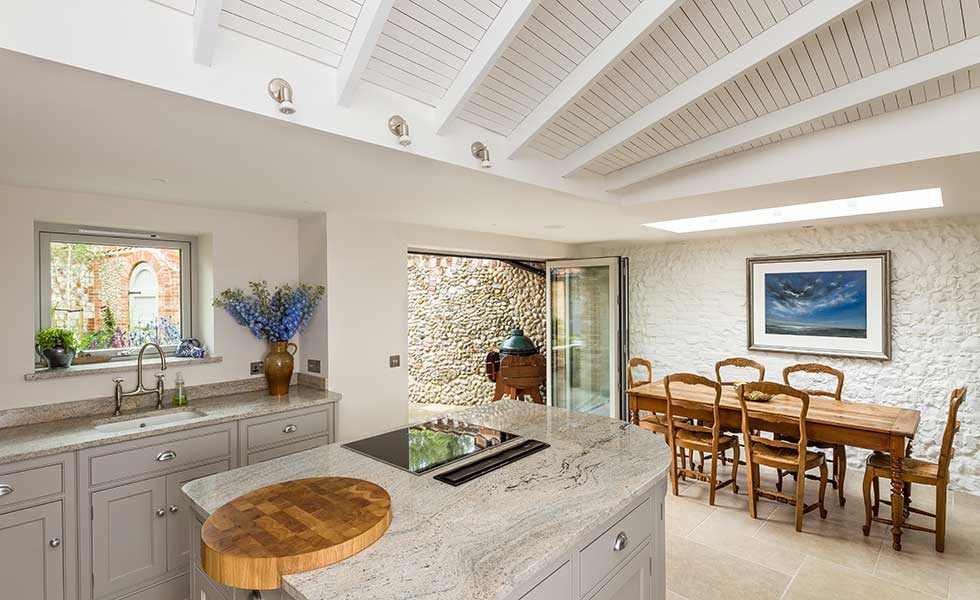 open plan kitchen with marble topped surfaces, wooden table and sliding doors