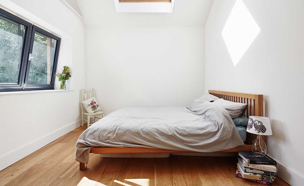 white bedroom with one large window, a wooden bed and grey bedding