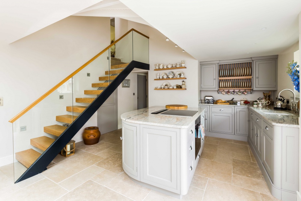 open plan kitchen with curved marble top kitchen counter and wood and glass staircase