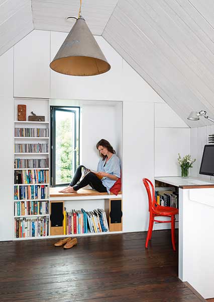 Clare Williamson sits in the window seat formed by built in storage in the loft room of a tiny efficient self build