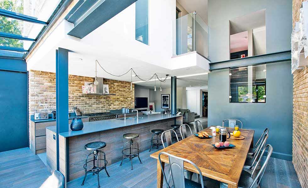 In this American loft-style self build in Surrey, the open plan kitchen/dining/living space is broken up into zones thanks to the jagged ceiling made up of varying levels. The kitchen sits under a lower ceiling while the dining space opposite boasts views up to the roof. Exposed steel beams and glazed mezzanines add to the jagged effect