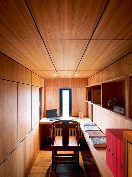 A low ceiling clad in timber to match the walls creates a cosy, enclosed space for a home office in this renovation project.