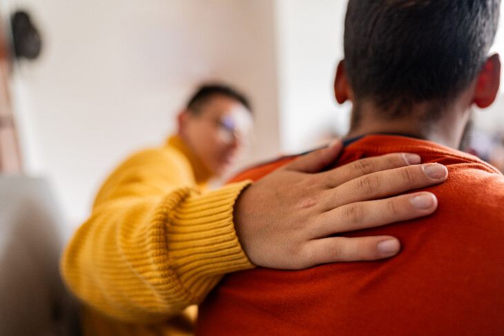 A man wearing a yellow jumper putting his arm around a man wearing a red top.