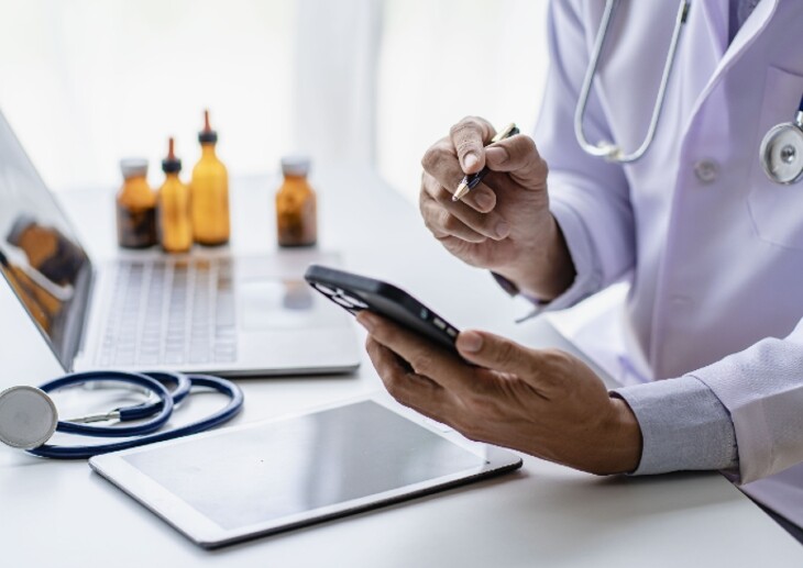 Doctor using mobile phone in a healthcare setting, with medicine bottles in the background