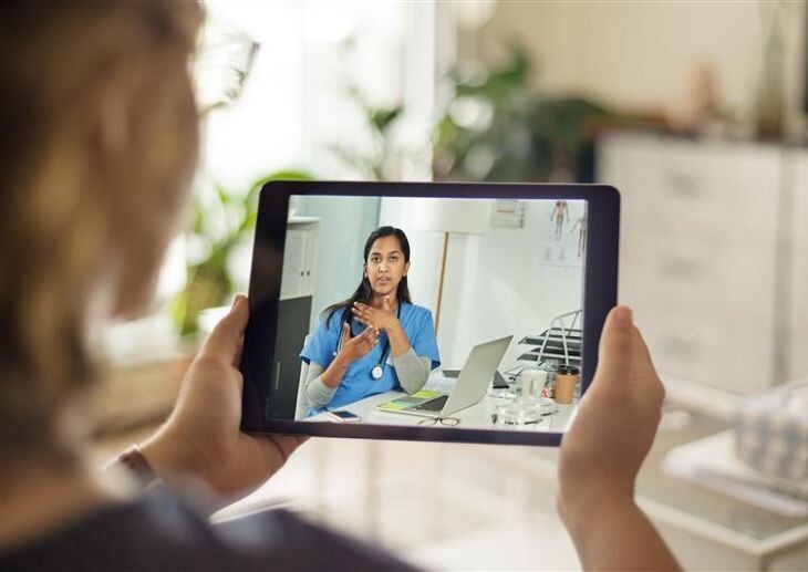 A patient holding a digital device with a doctor pictured on the device.