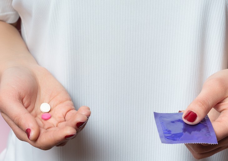 A woman wearing a white shirt, holding a condom and birth control pills in her hands