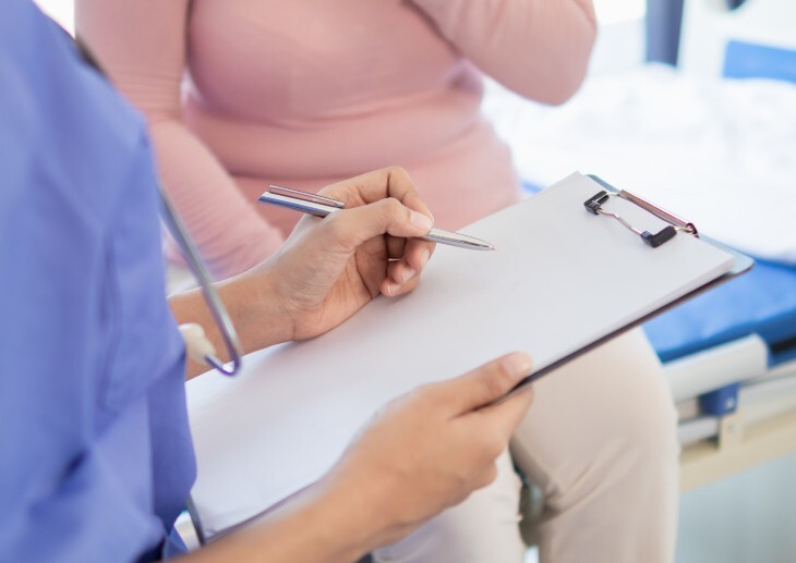 A nurse speaking with a patient and holding a clipboard.