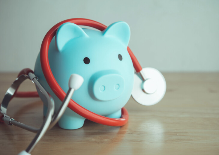 A stethoscope and a piggy bank on a table.