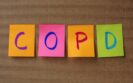 A line of an orange, pink, orange and green post-it notes with the letters COPD written on each one on a stripy brown background to illustrate the need to optimise medication-related support for COPD patients at hospital discharge
