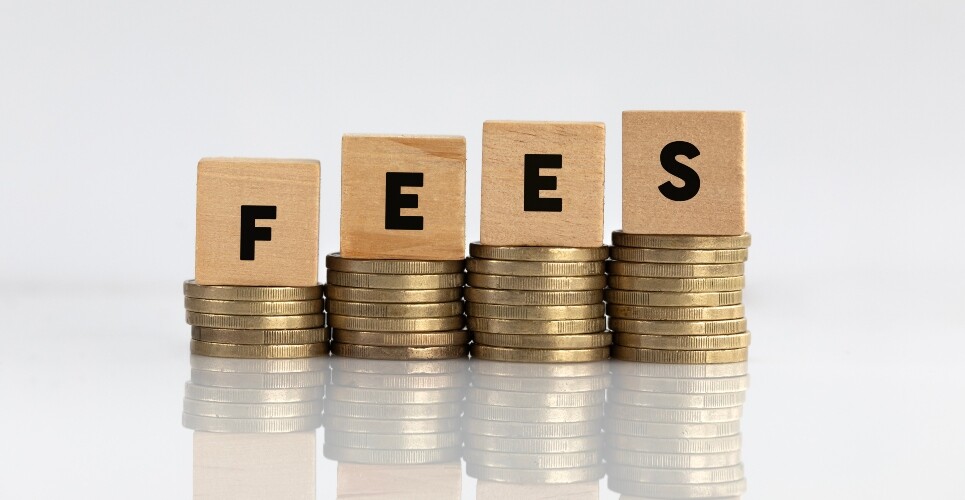 Four piles of coins increasing in size with a wooden block on top of each spelling out FEES to illustrate the GPhC confirming a 6% increase in fees from September but postponing its decision for 2026