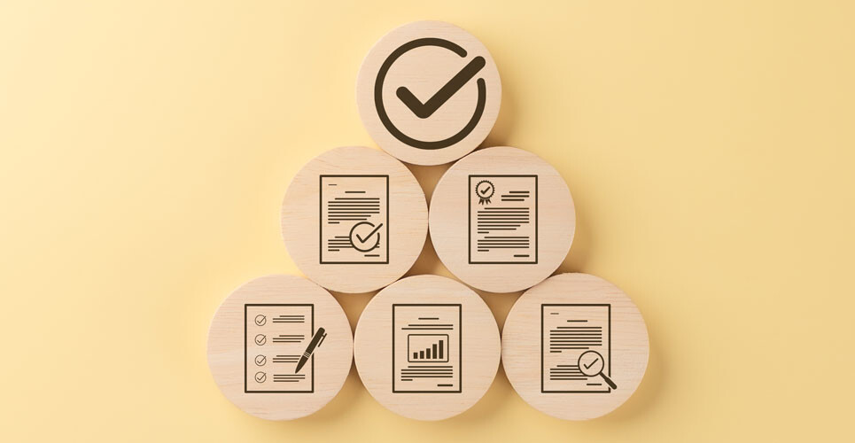 Wooden discs arranged in a pyramid with icons representing checklists, documents, certificates, charts, and a large tick in a circle at the top on a yellow background to illustrate an audit about the use of high-cost therapies such as dupilumab and JAK inhibitors for atopic dermatitis and adherence to NICE criteria for prescribing