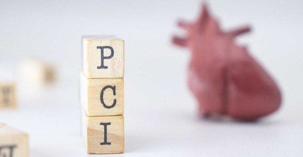 Three wooden blocks stacked on top of each other with the letters PCI on each one and a model of a human heart blurred in the background to illustrate the finding that early aspirin discontinuation and P2Y12 inhibitor monotherapy has benefits in low-risk MI patients after PCI