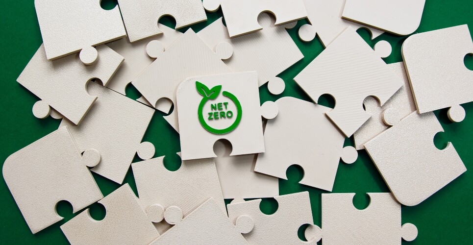 A pile of off-white jigsaw pieces on a green background with the words net zero in a circle with two leaves on the edge on the top piece to illustrate UCLH's sustainability progress and advice for clinicians to embrace their Trust green plan