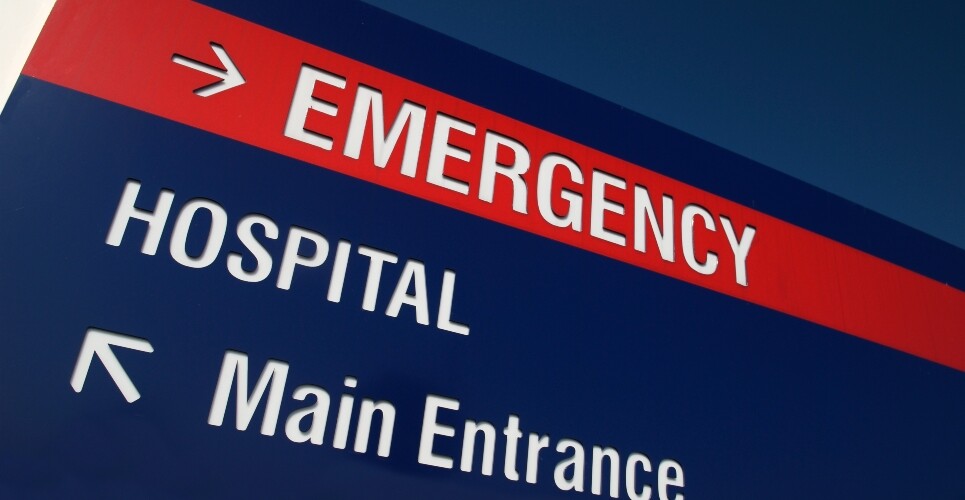 A close up of a navy blue hospital sign with a red stripe at the top saying emergency and an arrow pointing to the right, with the words hospital and main entrance underneath with an arrow pointing top left to illustrate the integration of pharmacists into the ED