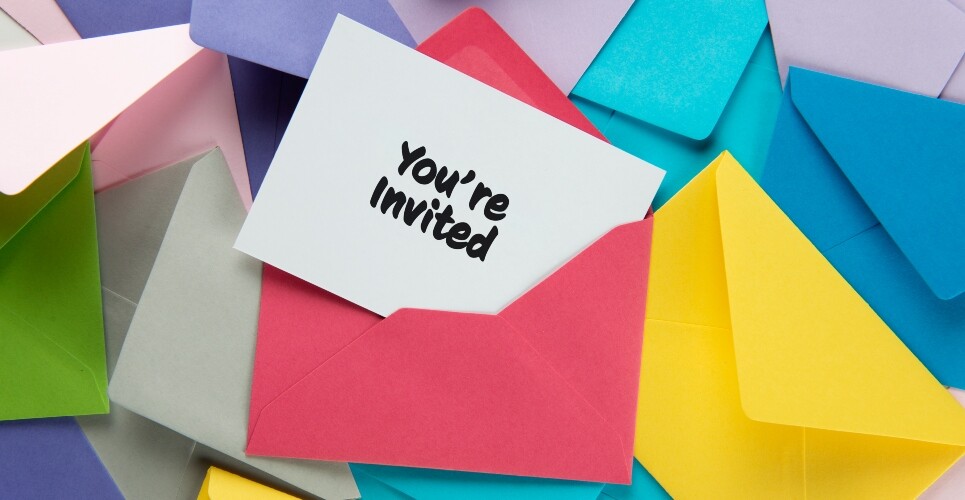 A selection of different coloured envelopes layered on top of each other and a pink one on top with a white card coming out of it showing the words you're invited to illustrate an invitation to join a focus group on automated unit-dose dispensing systems