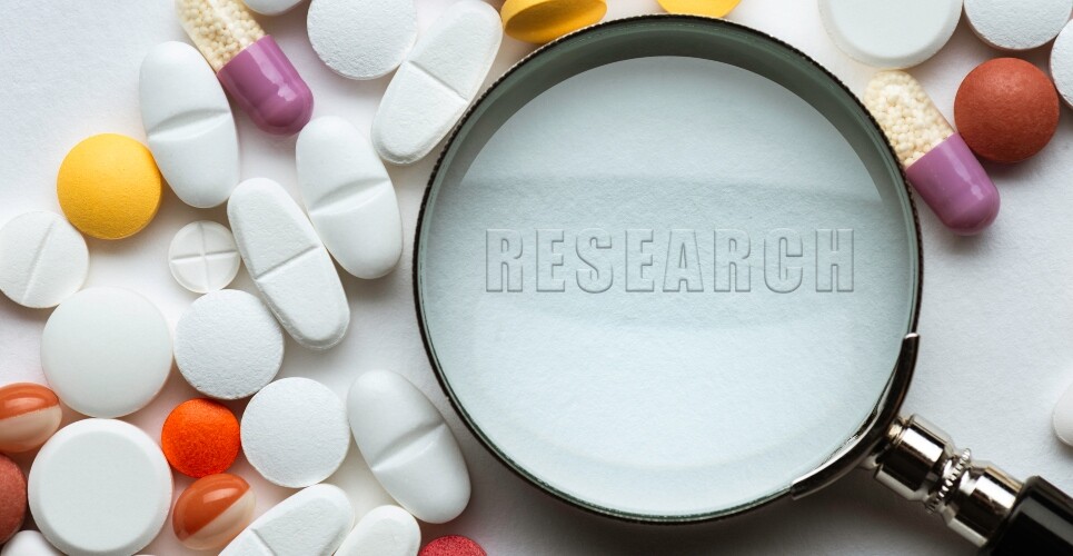A magnifying glass surrounded by different coloured tablets, capsules and pills and the word research in the centre to illustrate the work Stephen Tomlin is doing at GOSH to maximise hospital pharmacy and translate research into paediatric patient care