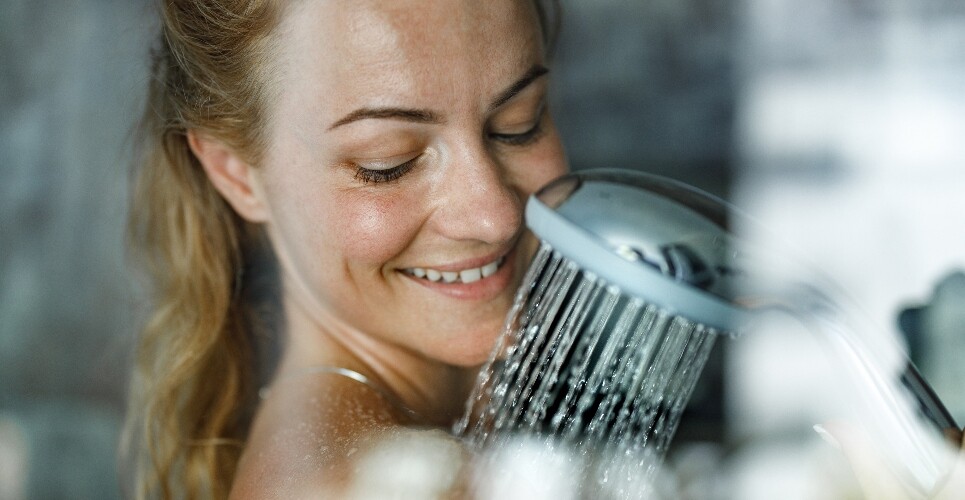 A close up of a smiling woman's head and shoulders while she is showering to illustrate the finding that eczema symptoms are unaffected by bathing frequency