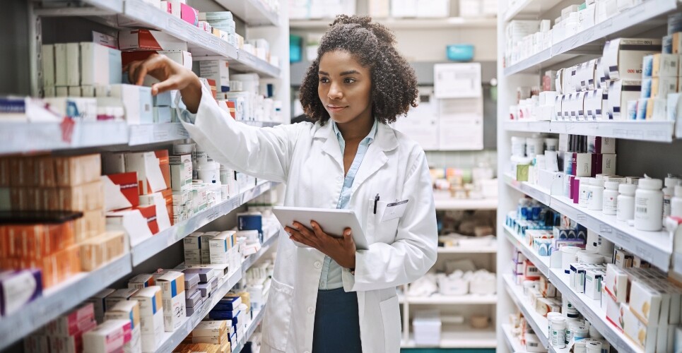 A young pharmacist holding an ipad in a hospital pharmacy dispensary to illustrate the launch of the 2025 RPS wellbeing survey for pharmacists and trainees