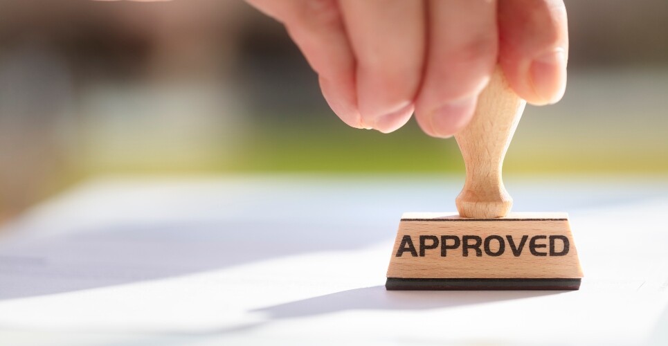A wooden stamp with the word approved on it being stamped on a piece of paper to illustrate the MHRA approval of the twice-yearly biologic depemokimab for the treatment of severe eosinophilic asthma and severe chronic rhinosinusitis with nasal polyps
