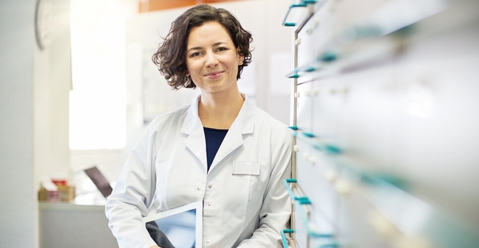 A pharmacist in a dispensary leaning against medication drawers and holding an iPad to illustrate the RPS calling for pharmacists to be at the heart of palliative care