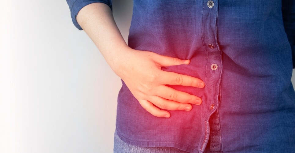 A close up of a woman holding her right hand side with a glowing red circle over the top of her hand to illustrate 10-year data showing antibiotics as viable for uncomplicated acute appendicitis in adults