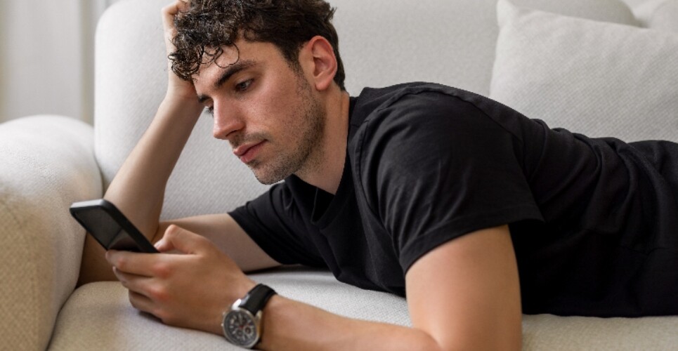 A young man laying on his front on a sofa looking at his smartphone to illustrate advice for recommending mental health apps and digital tools published by MHRA