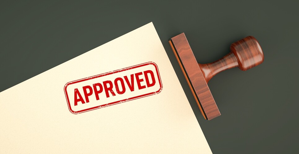 An approved stamp on the corner of a piece of paper with a wooden stamp laying next to it to illustrate deuruxolitinib being approved by the MHRA for severe alopecia areata