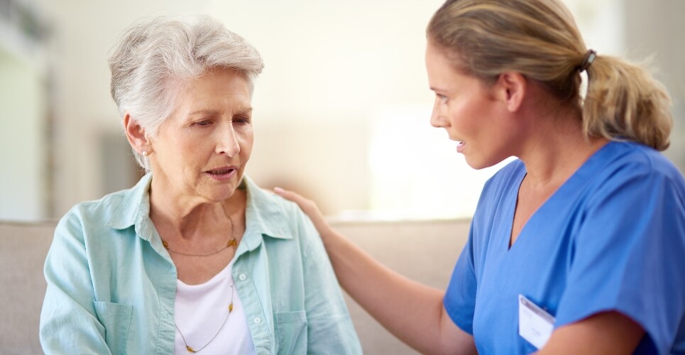 A clinician in scrubs comforting an old woman with Alzheimer's disease