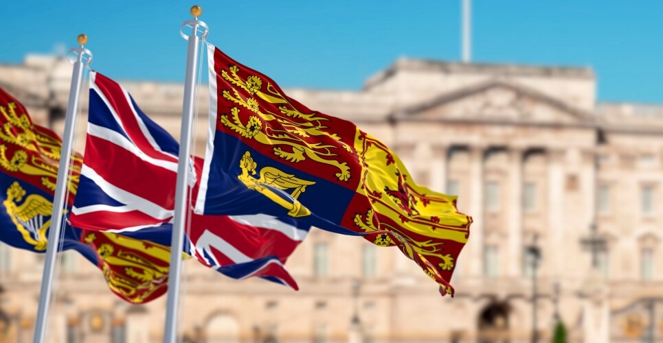 The Royal Standard of the United Kingdom waving with the UK flag with blurred Buckingham Palace in the background