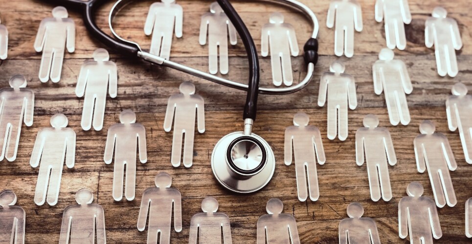 Stethoscope placed on a wooden surface surrounded by transparent human-shaped figures, symbolising healthcare, patient populations or clinical research
