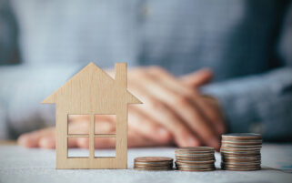 gp premises funding concept shown by wooden cut out of house with coins next to it