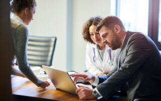supportive team shown by practice manager showing GP something on laptop