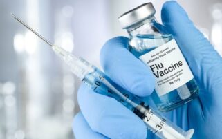 flu vaccine in vial alongside syringe