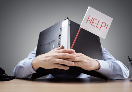 Digital transformation lead burying his head under a laptop asking for help with digital fatigue