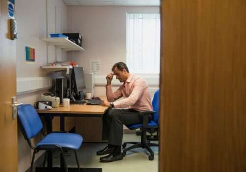 GP sitting at desk in consultation room which needs premises funding