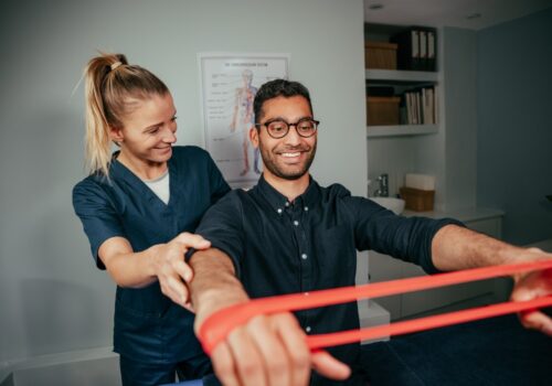 physiotherapist assisting male patient holding resistance band