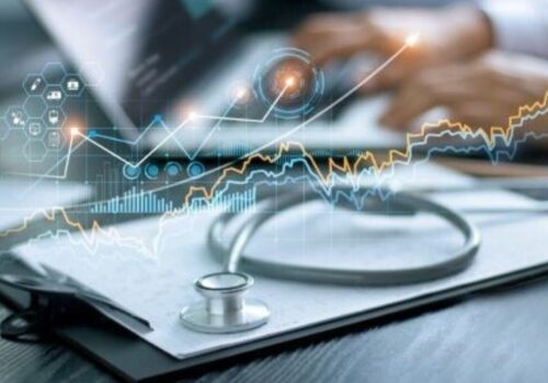 stethoscope resting on clipboard on a desk as medic looks at data on computer in background