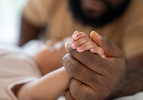 Close-up of a dad holding the hand of a baby