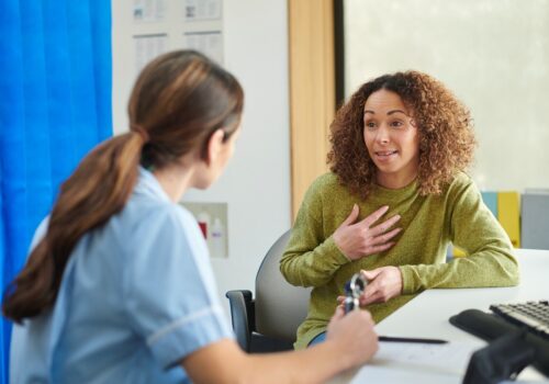A woman explaining her symptoms to a doctor in a GP surgery.