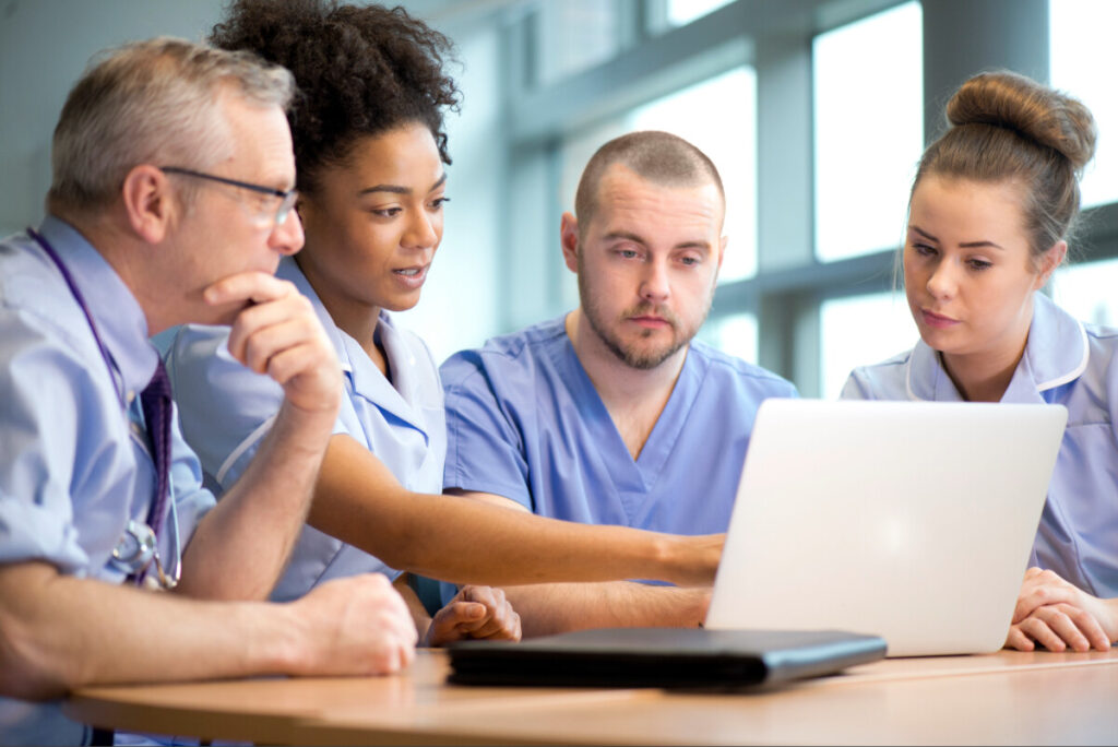 A group of GPs sitting at a desk and looking at a laptop.